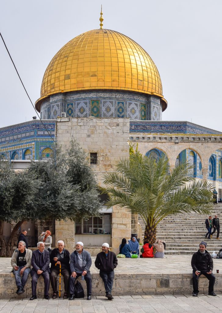 The Dome of the Rock in Jerusalem with people sitting nearby, showcasing iconic architecture.